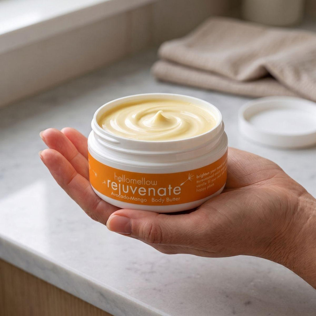 adult hand holding the rejuvenate body butter jar with the label facing forward
