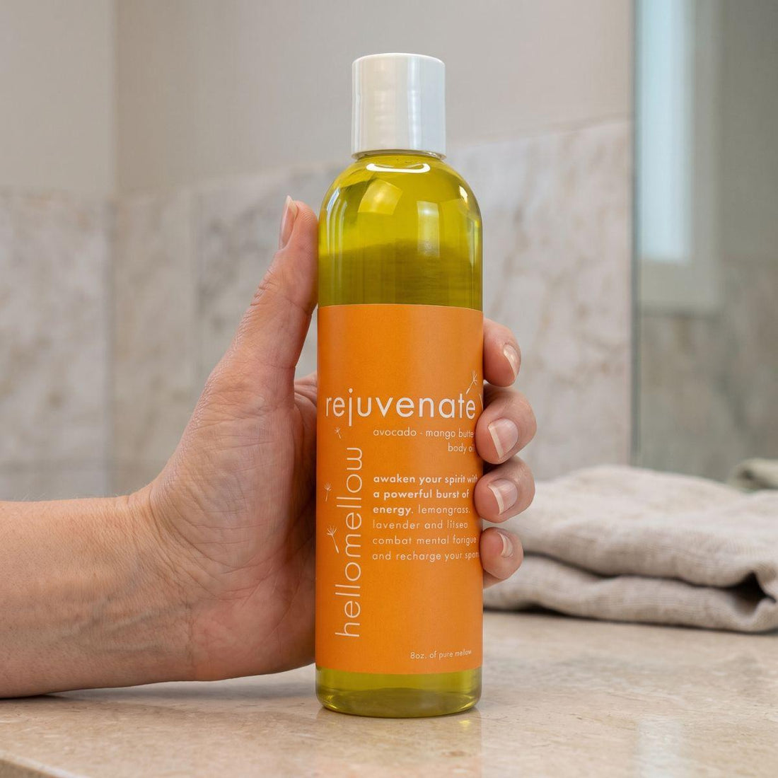 adult hand holding the rejuvenate body oil bottle with the label facing forward