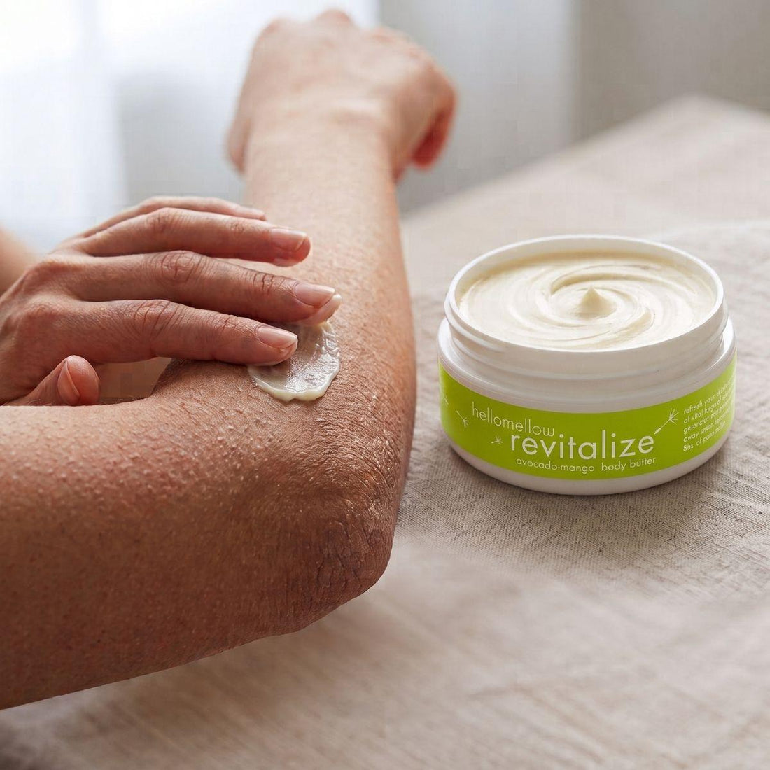 hands applying revitalize body butter to a dry elbow for targeted moisture