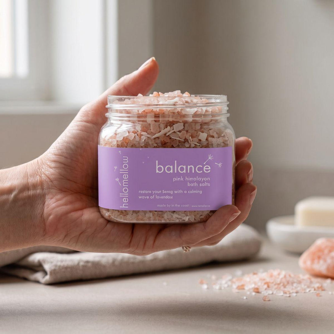 adult hand holding the balance bath salts jar with the label facing forward