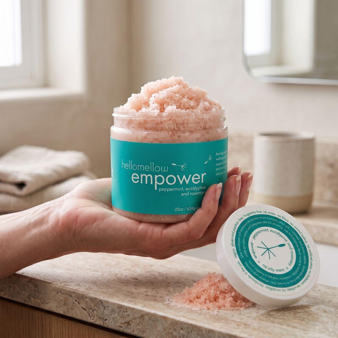 adult hand holding the empower body scrub jar with the label facing forward