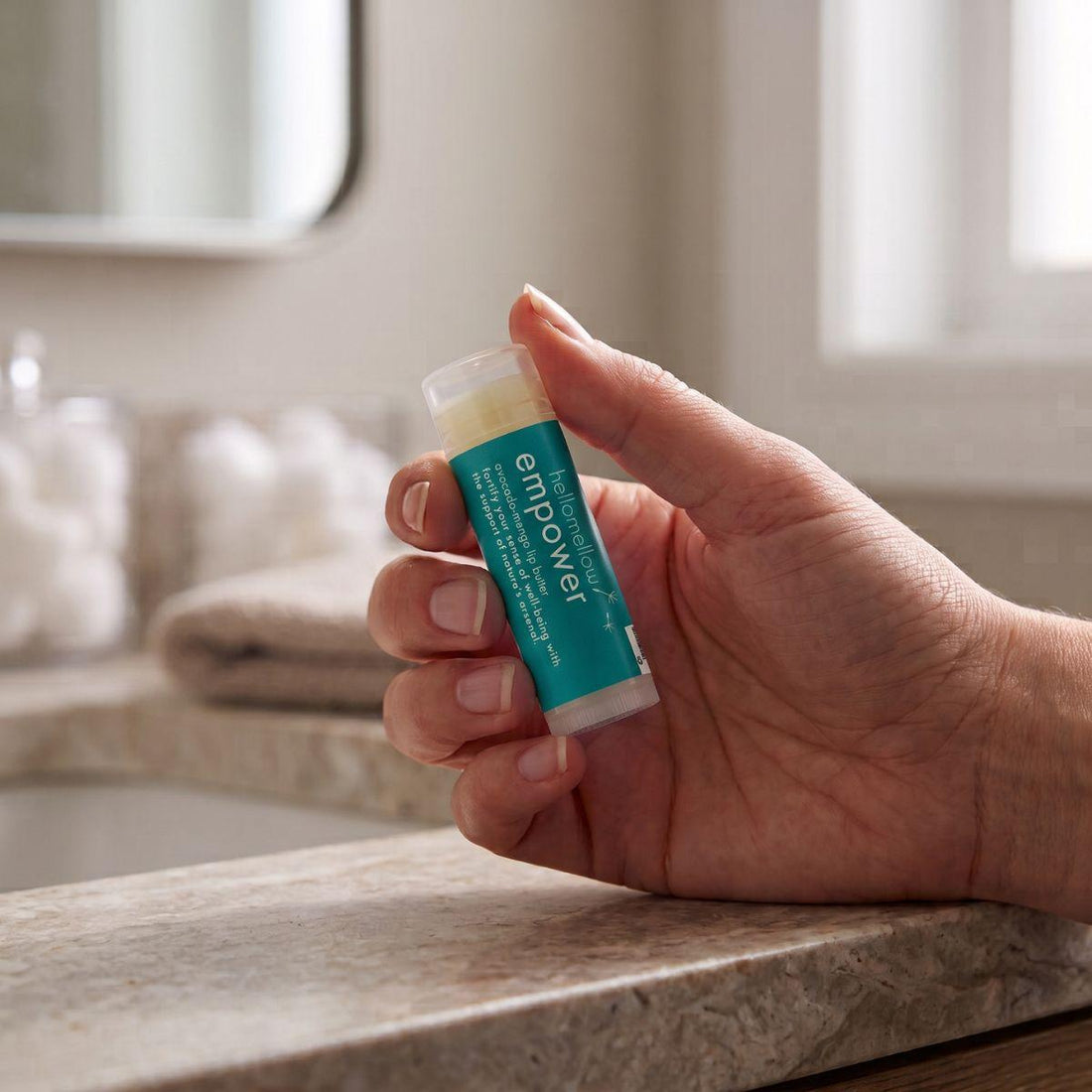 adult hand holding the empower lip butter to show its everyday size