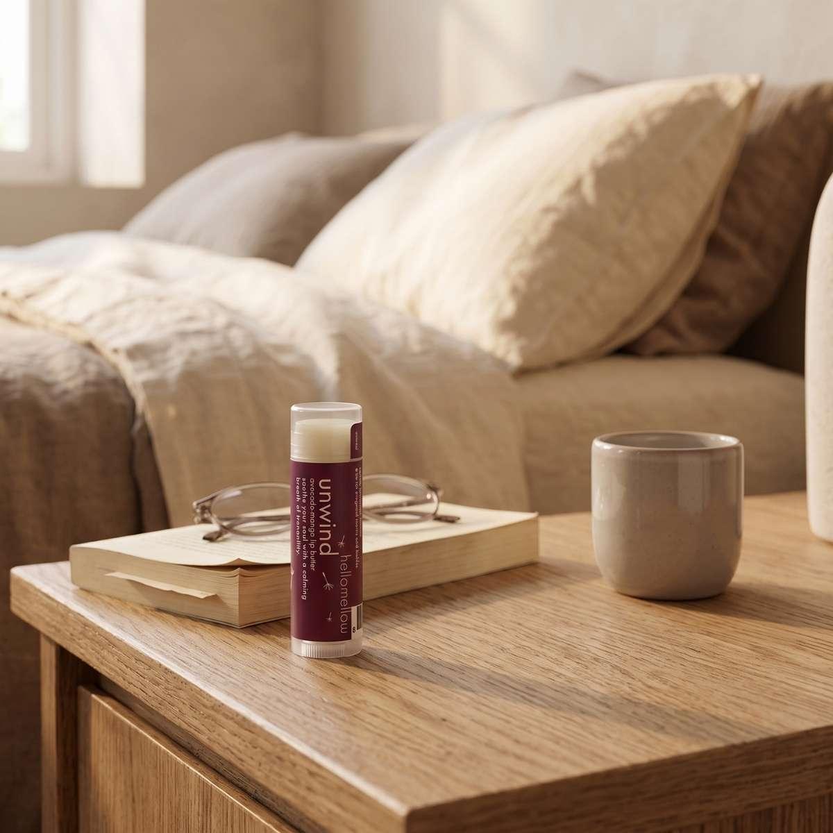 hellomellow unwind lip butter standing on a wooden nightstand next to reading glasses.