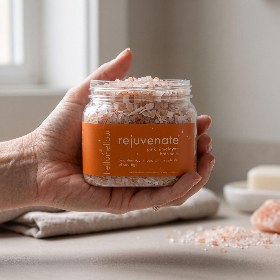 adult hand holding the rejuvenate bath salts jar with the label facing forward