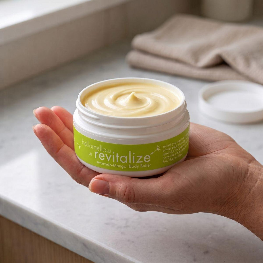 adult hand holding the revitalize body butter jar with the label facing forward