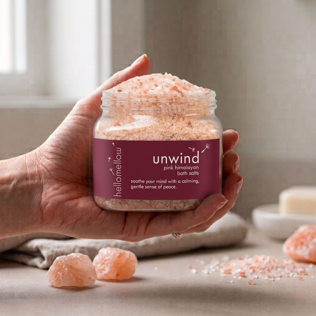 adult hand holding the unwind bath salts jar with the label facing forward