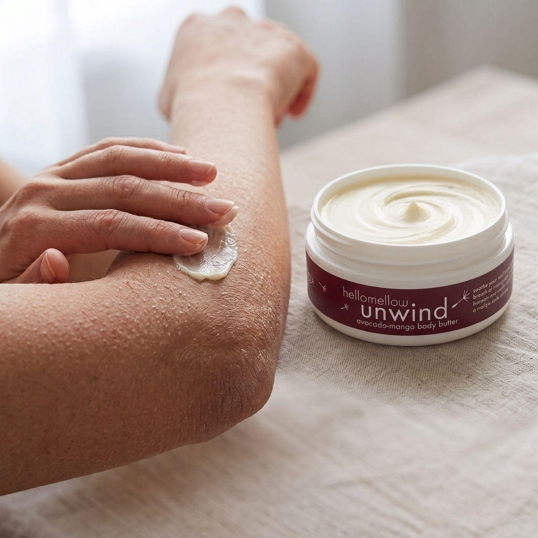 hands applying unwind body butter to a dry elbow for targeted moisture