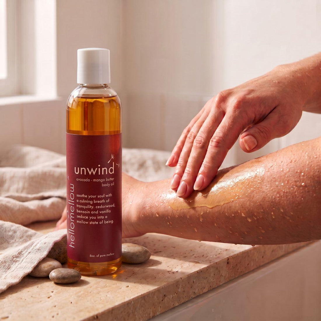 hands smoothing unwind body oil onto damp skin after a shower