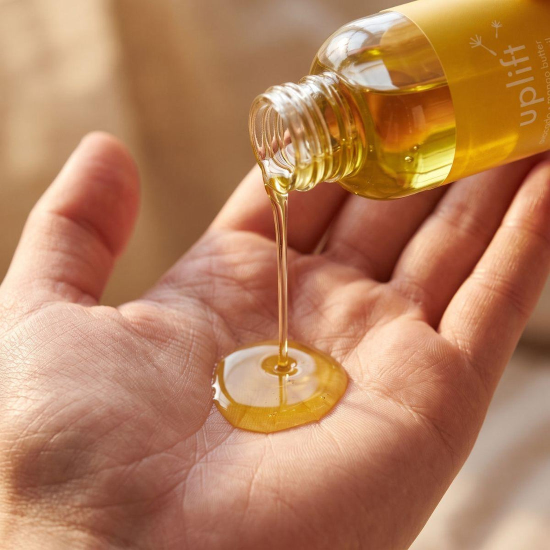 uplift body oil pouring into an open palm with the bottle nearby